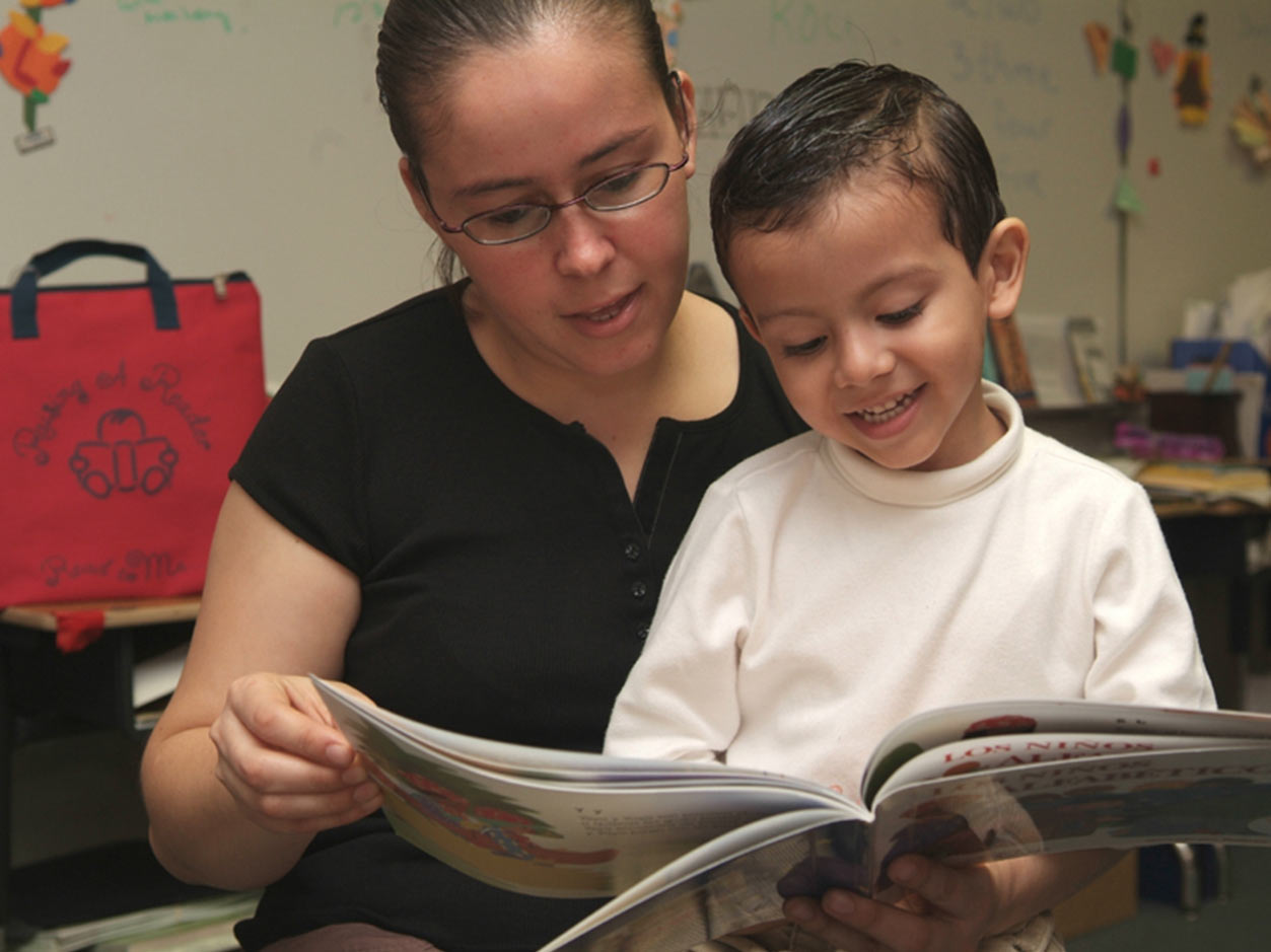 an image of a woman with a small child on her lap while she reads him a book inside their home