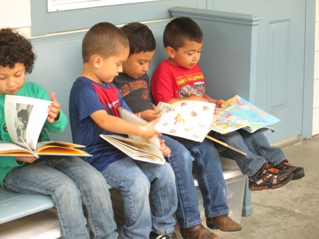 an image of children sitting on a bench reading large childrens books together